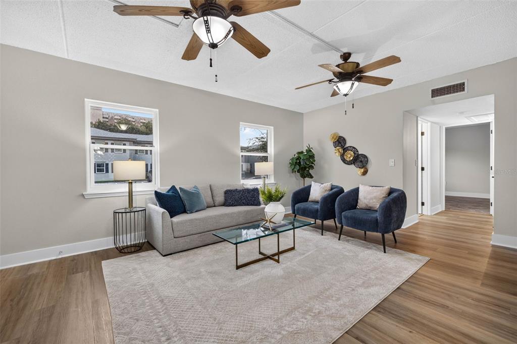 A living room features a gray sofa, two blue armchairs, and two ceiling fans — 1190 RUE DES CHATEAUX UNIT 1A, ST PETERSBURG, FL