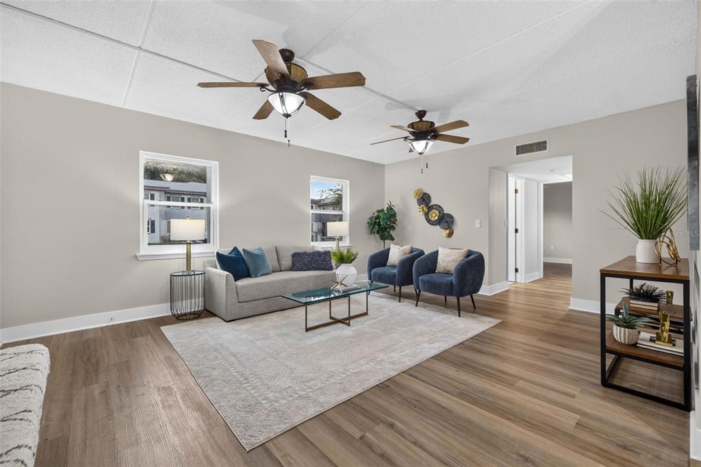 A living room features light gray walls, wood-look flooring, two ceiling fans, and modern furniture — 1190 RUE DES CHATEAUX UNIT 1A, ST PETERSBURG, FL