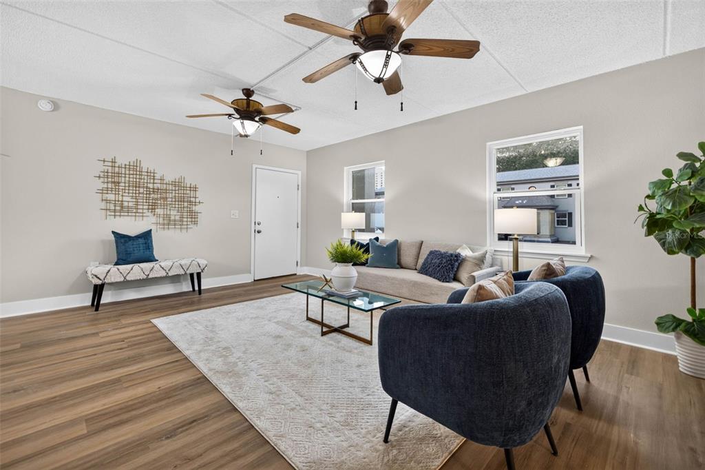 A living room features wood-look flooring, two ceiling fans, a sofa, and two blue chairs — 1190 RUE DES CHATEAUX UNIT 1A, ST PETERSBURG, FL