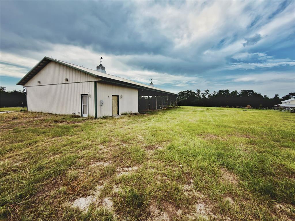 A large metal barn with two doors stands in a grassy field under a cloudy sky — 24087 TWISTER LANE, BROOKSVILLE, FL