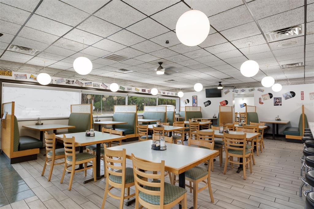 A restaurant dining room features multiple tables, green booths, wooden chairs, and globe pendant lights — 5300 E SILVER SPRINGS BOULEVARD UNIT B, SILVER SPRINGS, FL