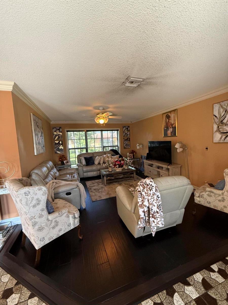A room with dark wood-look flooring, tan walls, a ceiling fan, and a large window — 511 SW 63rd Terrace, Margate FL 33068, MARGATE, FL