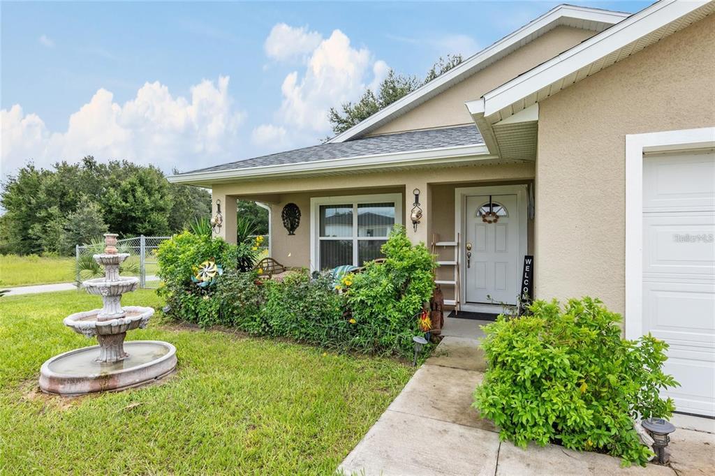A tan house exterior features a front porch, a tiered fountain, and a white door — 4660 SW 130TH STREET, OCALA, FL