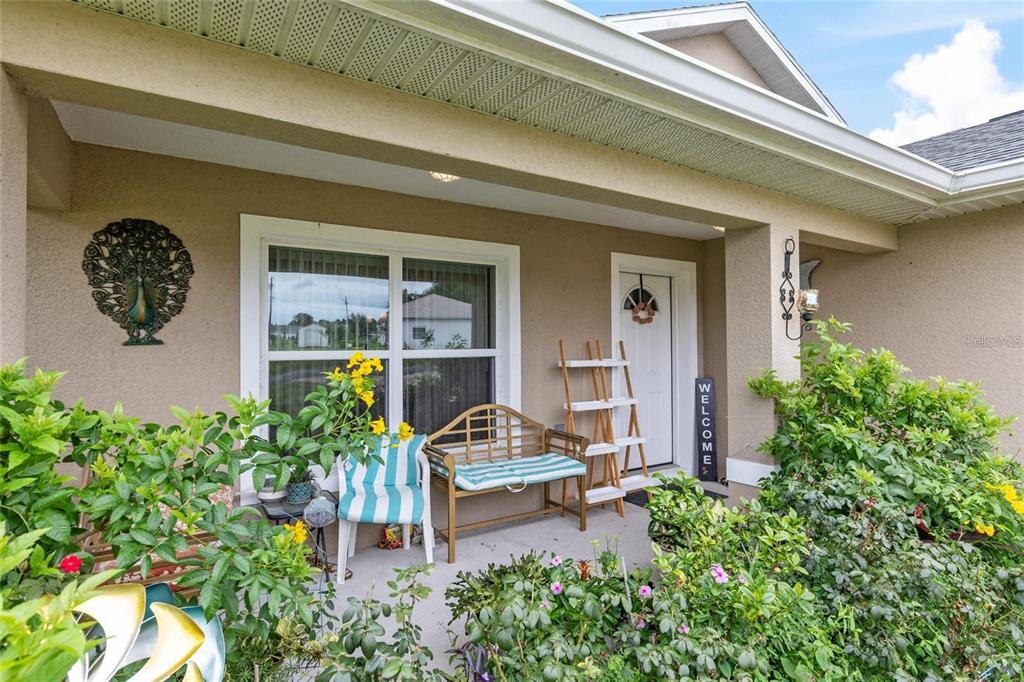 A covered front porch features a wooden bench, a tiered plant stand, and decorative wall art — 4660 SW 130TH STREET, OCALA, FL