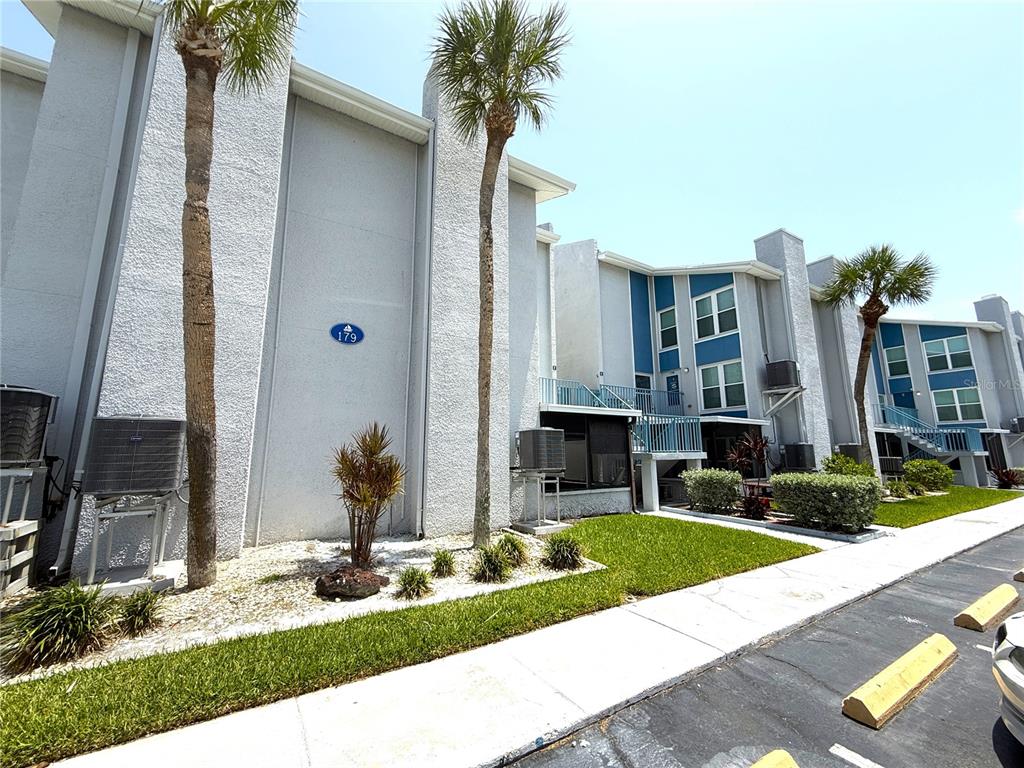 A multi-story apartment building exterior with light gray stucco walls and palm trees — 179 MEDALLION BLVD UNIT C, MADEIRA BEACH, FL
