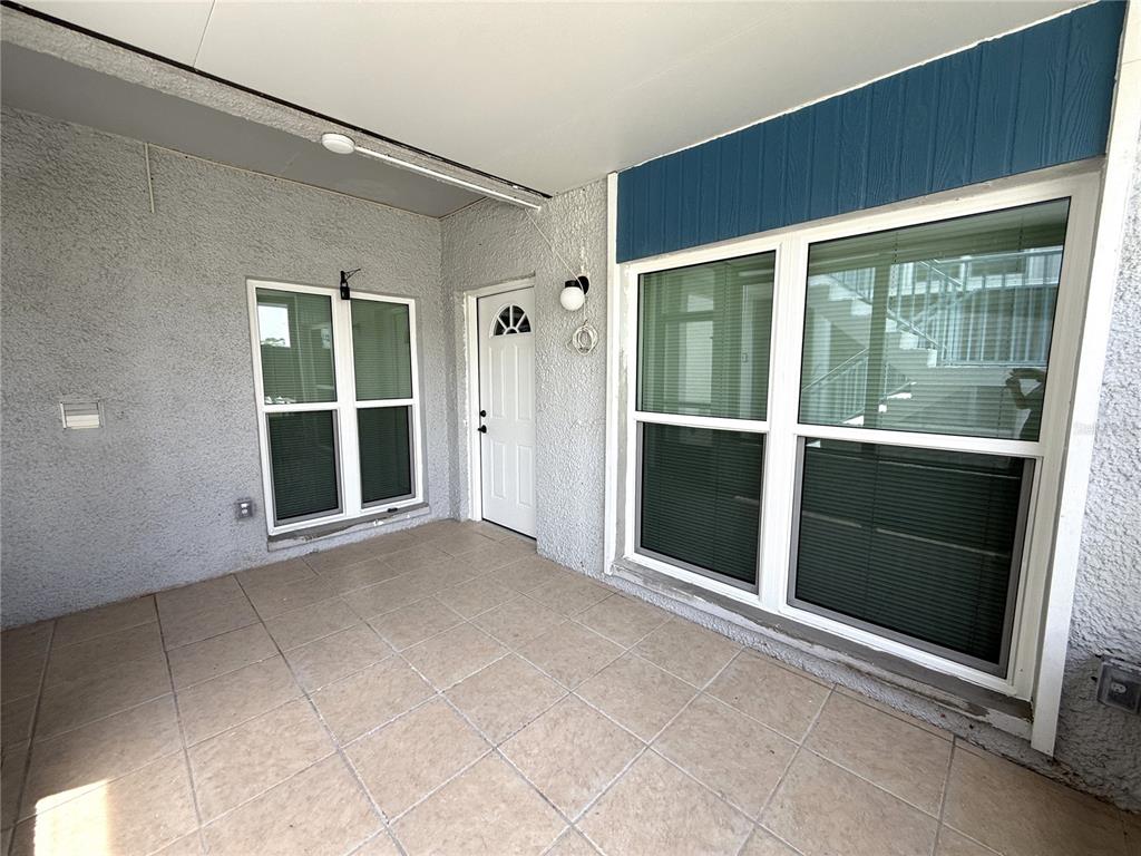 A covered patio features light-colored tile flooring, stucco walls, a white door, and large windows — 179 MEDALLION BLVD UNIT C, MADEIRA BEACH, FL