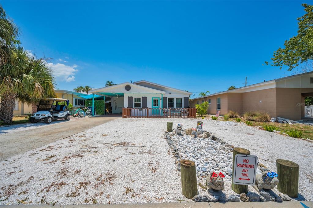 A white brick house with a wooden fence and a gravel driveway under a blue sky — 305 15TH AVENUE, INDIAN ROCKS BEACH, FL