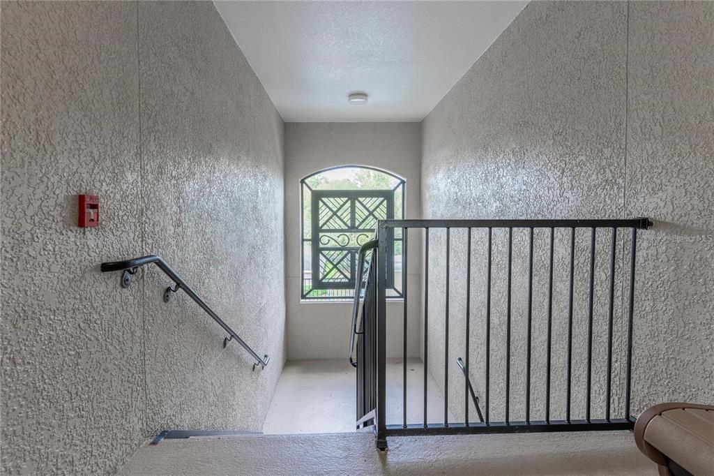 A stairwell landing features textured walls, a metal railing, and an arched window — 3583 CONROY ROAD UNIT 1135, ORLANDO, FL
