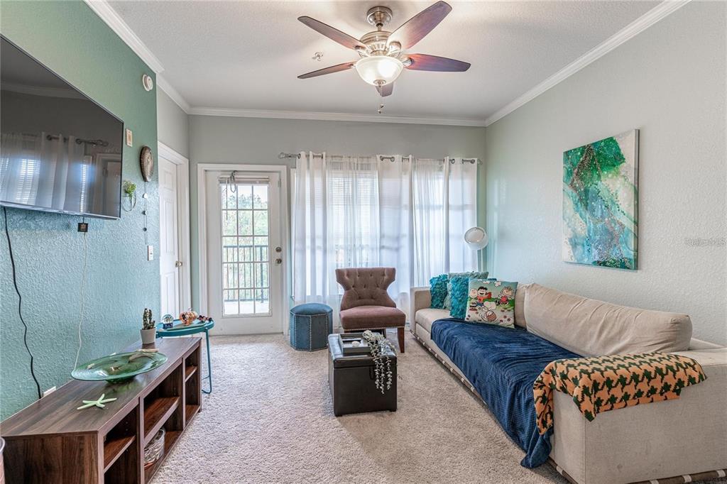 A living room features a beige sofa, a television, a ceiling fan, and a balcony door — 3583 CONROY ROAD UNIT 1135, ORLANDO, FL