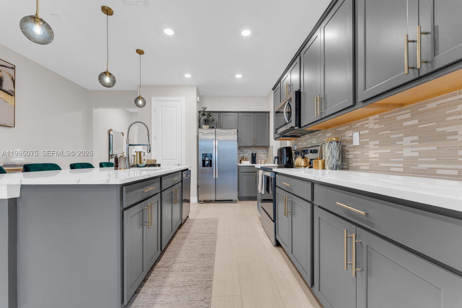 A modern kitchen features gray cabinets, white countertops, stainless steel appliances, and pendant lighting — 8351 NW 7th Ct, Plantation FL 33324, PLANTATION, FL