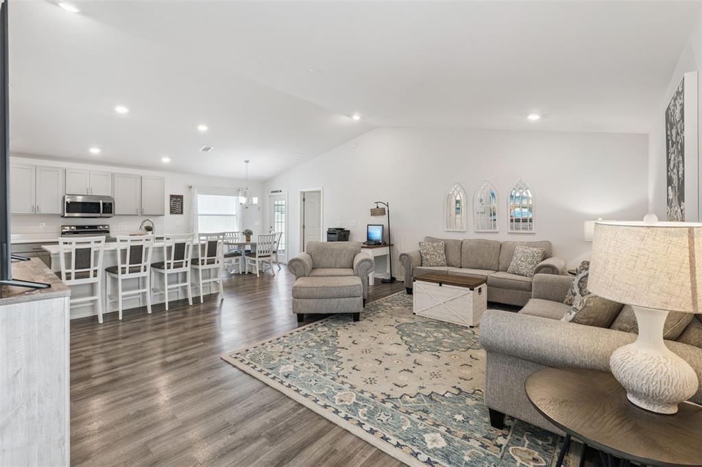 An open-concept living room and kitchen feature gray cabinetry, wood-look flooring, and neutral furniture — 5604 MADDIE DRIVE, HAINES CITY, FL