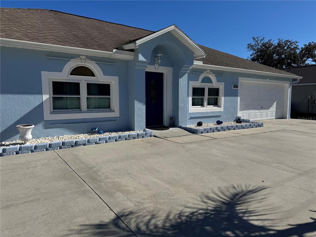 A light blue single-story house features a dark front door, white trim, and a concrete driveway — 303 BACCARAT COURT, KISSIMMEE, FL