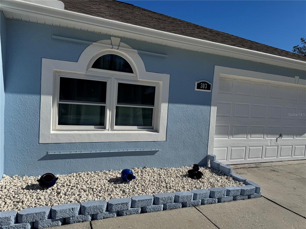 The exterior of a light blue house features a decorative window and a garage door — 303 BACCARAT COURT, KISSIMMEE, FL