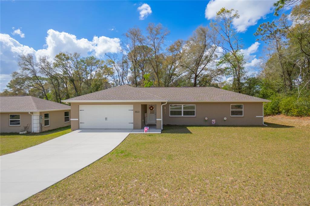 A single-story house with a tan exterior, white garage door, and a concrete driveway — 3522 S OAKDALE TERRACE, INVERNESS, FL