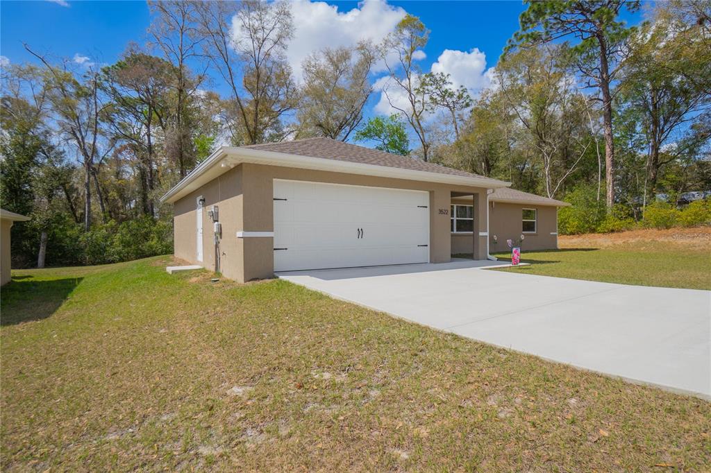 A tan stucco house features a white two-car garage and a concrete driveway — 3522 S OAKDALE TERRACE, INVERNESS, FL