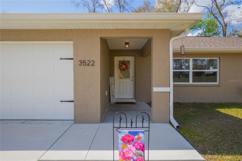 The exterior view shows a tan house with a white garage door and front entrance — 3522 S OAKDALE TERRACE, INVERNESS, FL
