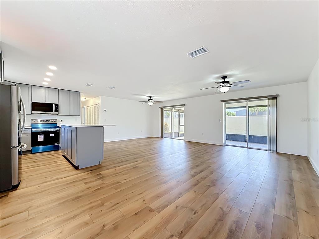 A bright, open-concept living area features light wood-look flooring, a kitchen island, and sliding doors — 2188 CORINNE COURT S UNIT A, ST PETERSBURG, FL