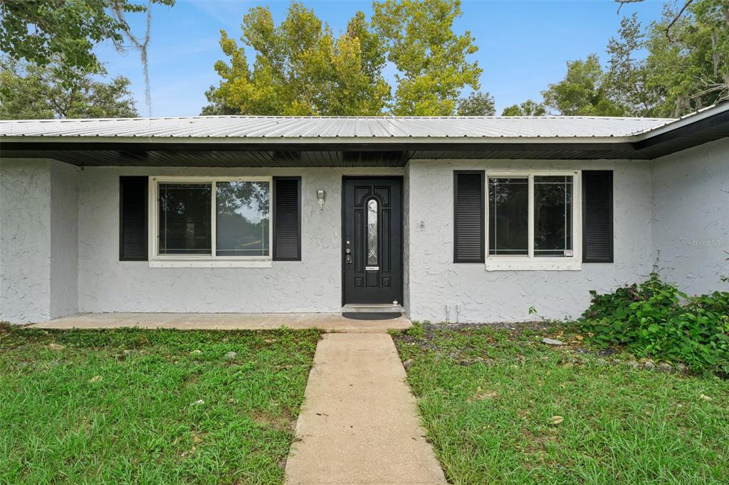 A single-story house with a white stucco exterior, black shutters, and a metal roof — 2142 KENDALL COURT, DELTONA, FL