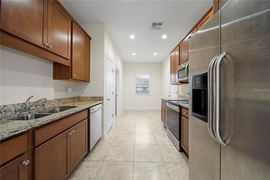 A galley kitchen features wood cabinets, granite countertops, stainless steel appliances, and tile flooring — 14 FERGUSON DRIVE, ORLANDO, FL