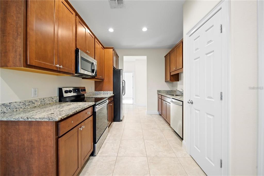 A galley-style kitchen features wood cabinets, granite countertops, stainless steel appliances, and tile flooring — 14 FERGUSON DRIVE, ORLANDO, FL