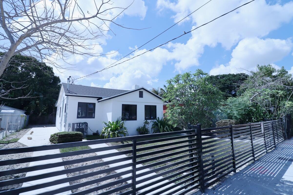 A white house with a dark roof and black trim sits behind a horizontal slat fence — 3040 NW 13th Avenue # 1, Miami FL 33142, MIAMI, FL