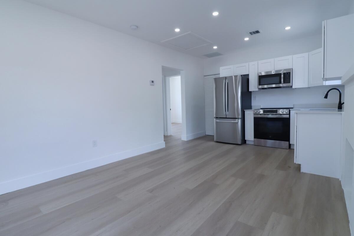 A modern kitchen with white cabinets and stainless steel appliances opens to a living area — 3040 NW 13th Avenue # 1, Miami FL 33142, MIAMI, FL