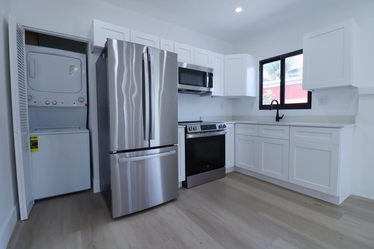 A kitchen with white cabinets, stainless steel appliances, and a stacked washer and dryer unit — 3040 NW 13th Avenue # 1, Miami FL 33142, MIAMI, FL