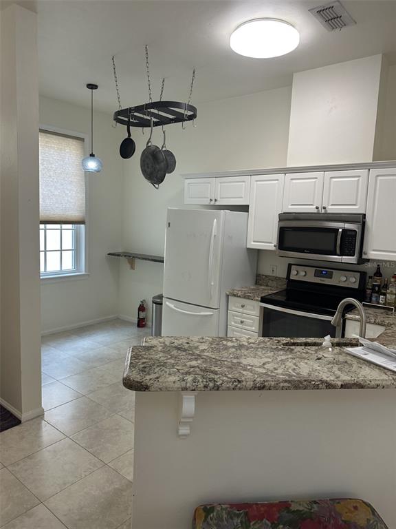 A kitchen features white cabinets, granite countertops, a hanging pot rack, and tile flooring — 5202 SW 91ST TERRACE UNIT B, GAINESVILLE, FL