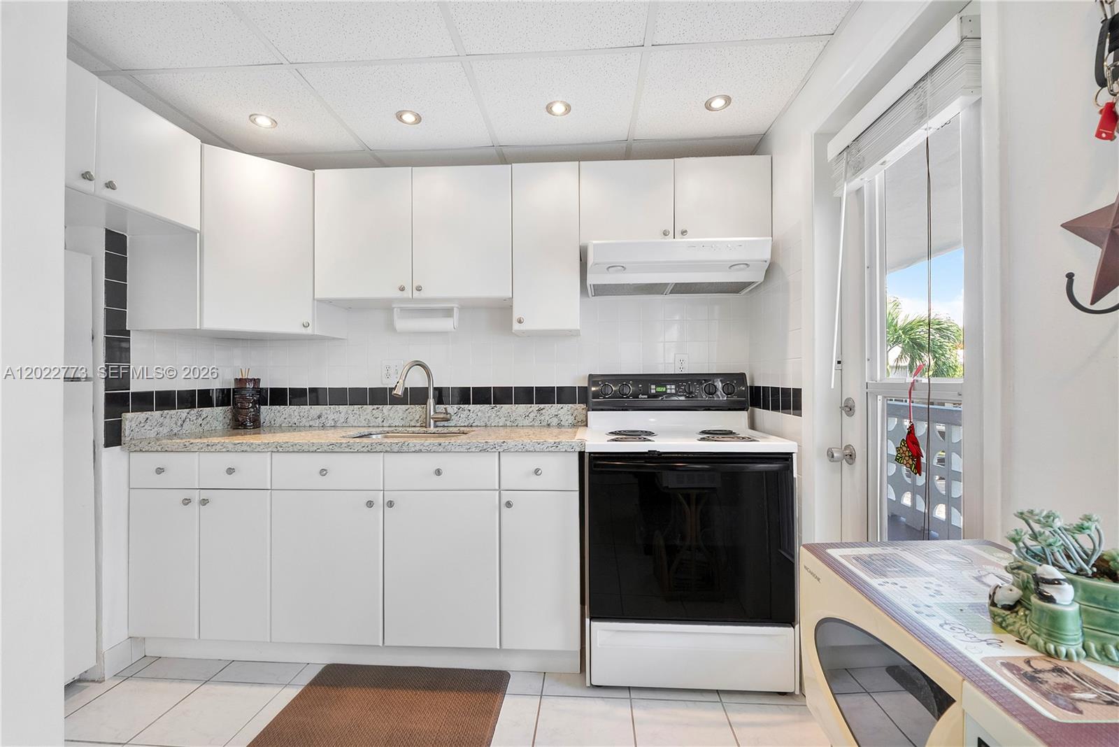 A kitchen features white cabinets, granite countertops, a black-and-white tiled backsplash, and a glass door — 3133 S Ocean Dr # 318, Hallandale Beach FL 33009, HALLANDALE BEACH, FL