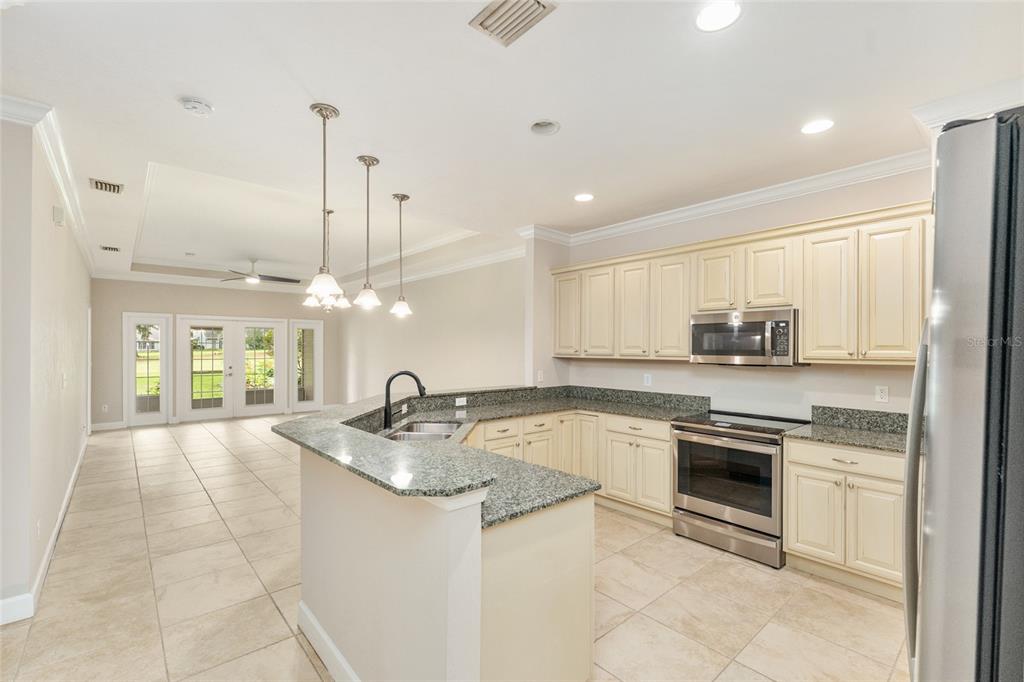 A kitchen with cream cabinets, granite countertops, and stainless steel appliances overlooks an open living area — 12705 NW 11TH PLACE, NEWBERRY, FL