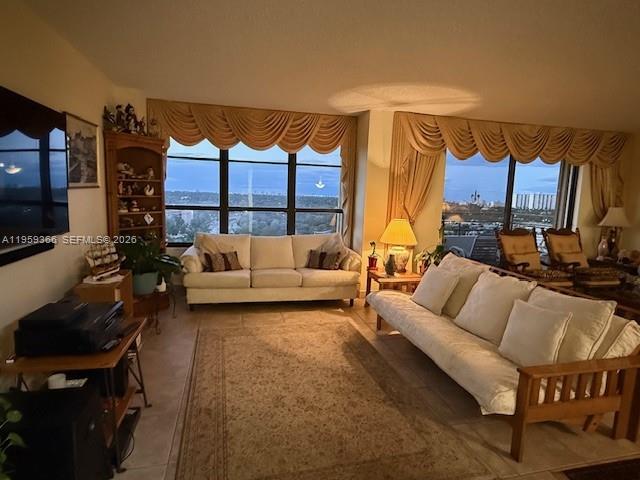 A living room features a beige sofa, a wooden futon, and large windows with valances — 600 Three Islands Blvd # 1004, Hallandale Beach FL 33009, HALLANDALE BEACH, FL