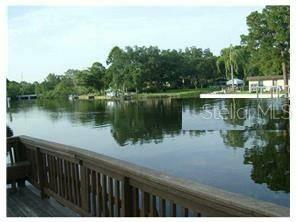 A wooden deck overlooks a calm lake surrounded by trees and residential properties — 9110 TUDOR DRIVE UNIT L106, TAMPA, FL
