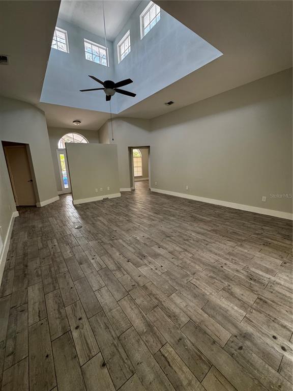 A spacious living room features high ceilings, a ceiling fan, and wood-look tile flooring — 1645 17TH STREET SW, NAPLES, FL