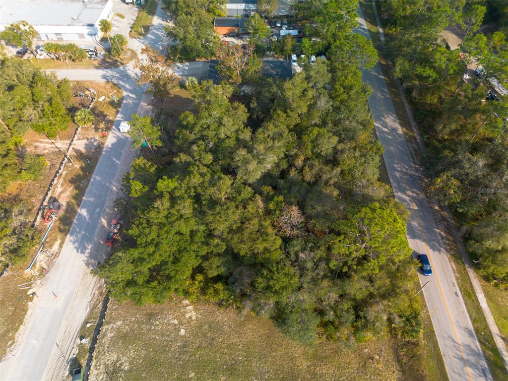 An aerial view shows a wooded, undeveloped lot situated between two paved roads — 290 S INDUSTRIAL DRIVE, ORANGE CITY, FL