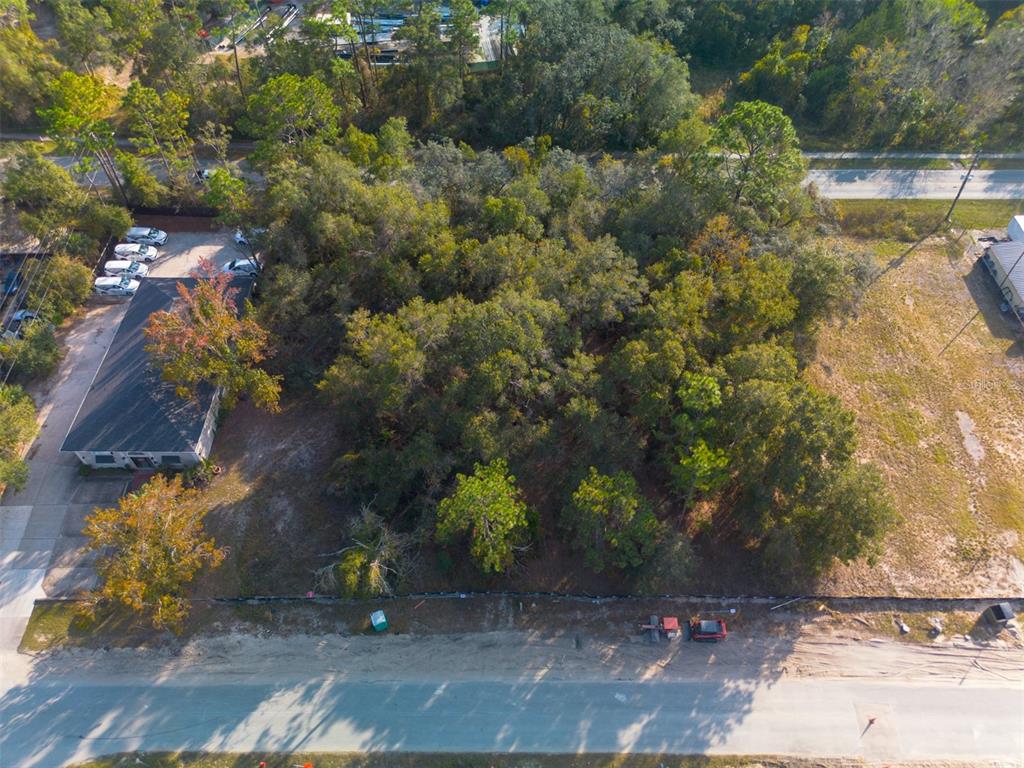 An aerial view shows a wooded lot situated between a commercial building and an open field — 290 S INDUSTRIAL DRIVE, ORANGE CITY, FL