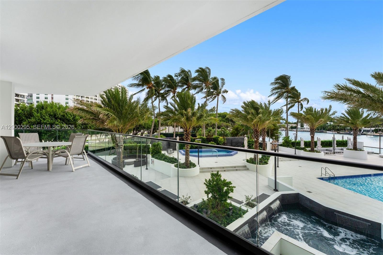 A balcony overlooks a swimming pool, a hot tub, and palm trees near a waterway — 5500 Collins Ave # 304, Miami Beach FL 33140, MIAMI BEACH, FL