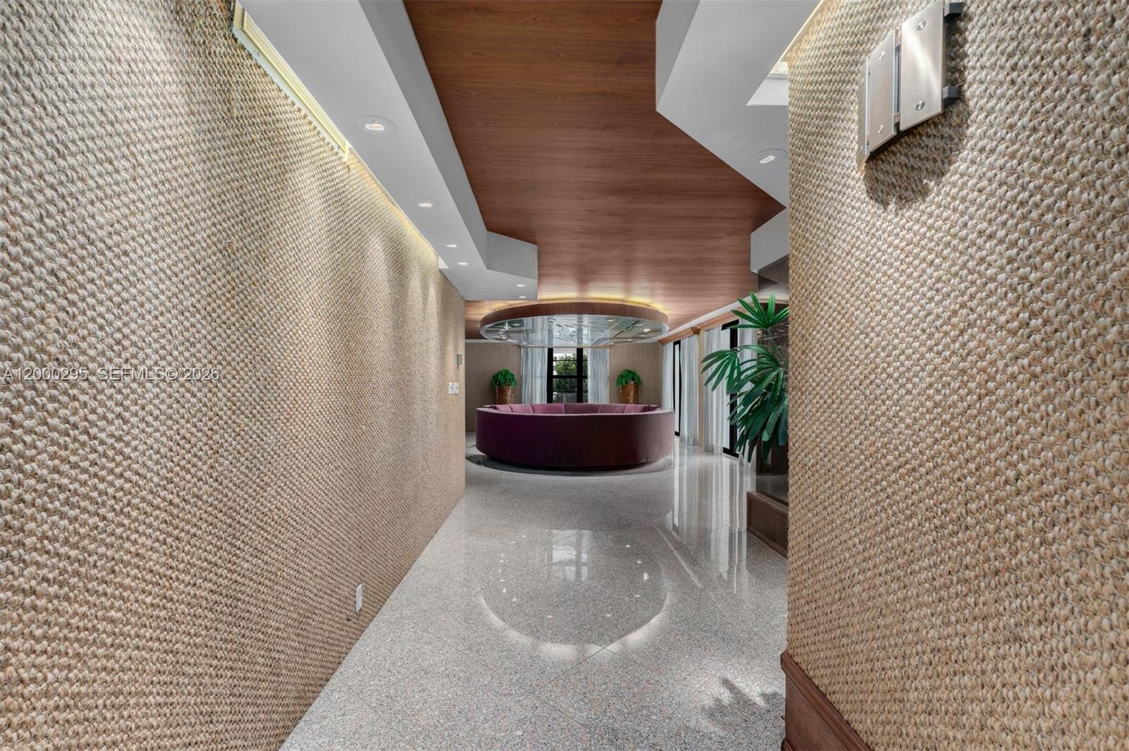 A hallway with textured walls and a wood-paneled ceiling leads to a circular seating area — 5500 Collins Ave # 304, Miami Beach FL 33140, MIAMI BEACH, FL
