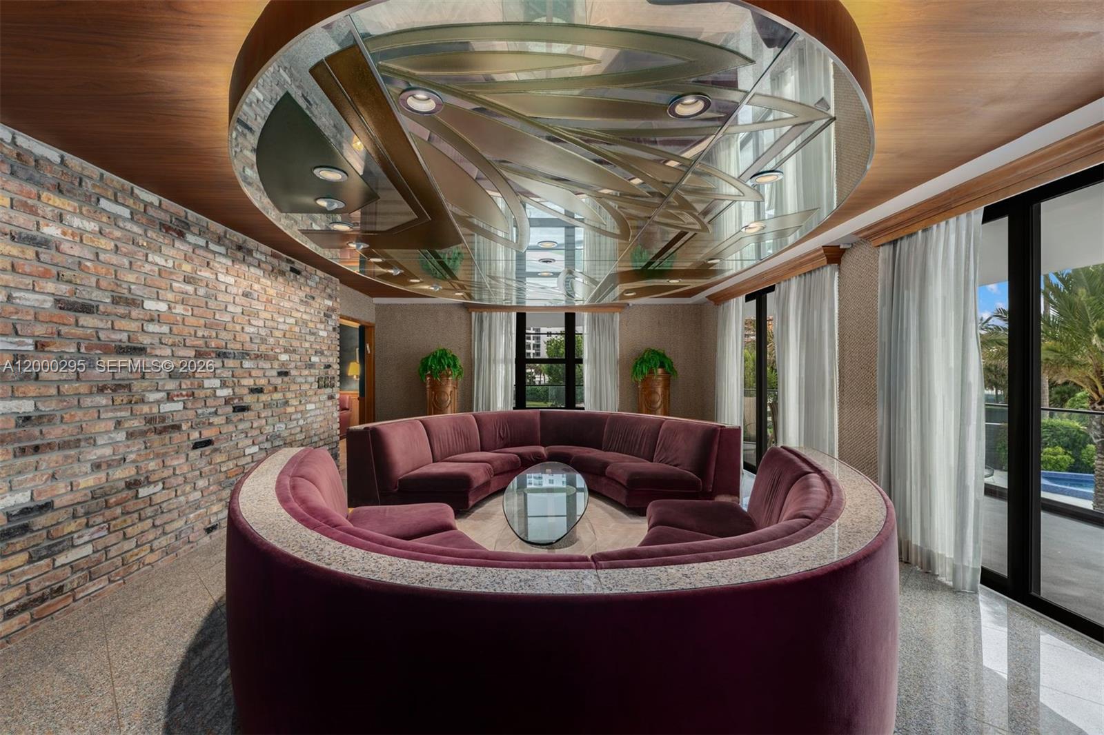 A circular conversation pit with velvet seating sits beneath a decorative mirrored ceiling in a room — 5500 Collins Ave # 304, Miami Beach FL 33140, MIAMI BEACH, FL