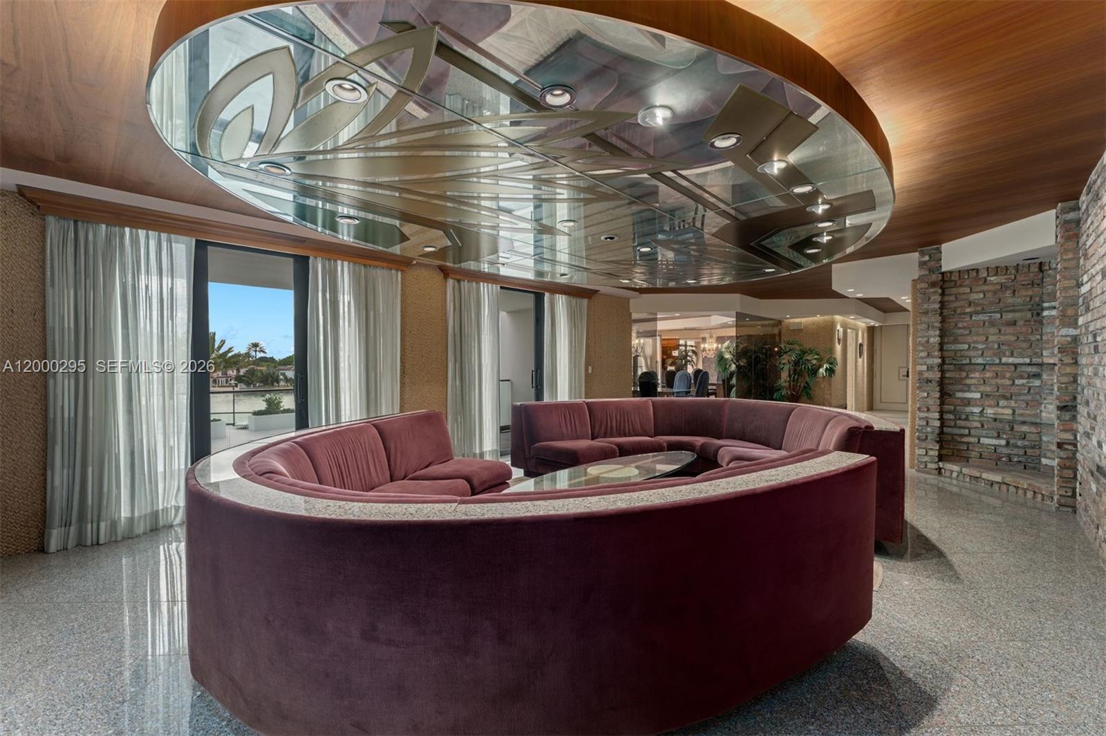 A circular velvet sofa sits beneath a decorative mirrored ceiling in a modern living room — 5500 Collins Ave # 304, Miami Beach FL 33140, MIAMI BEACH, FL