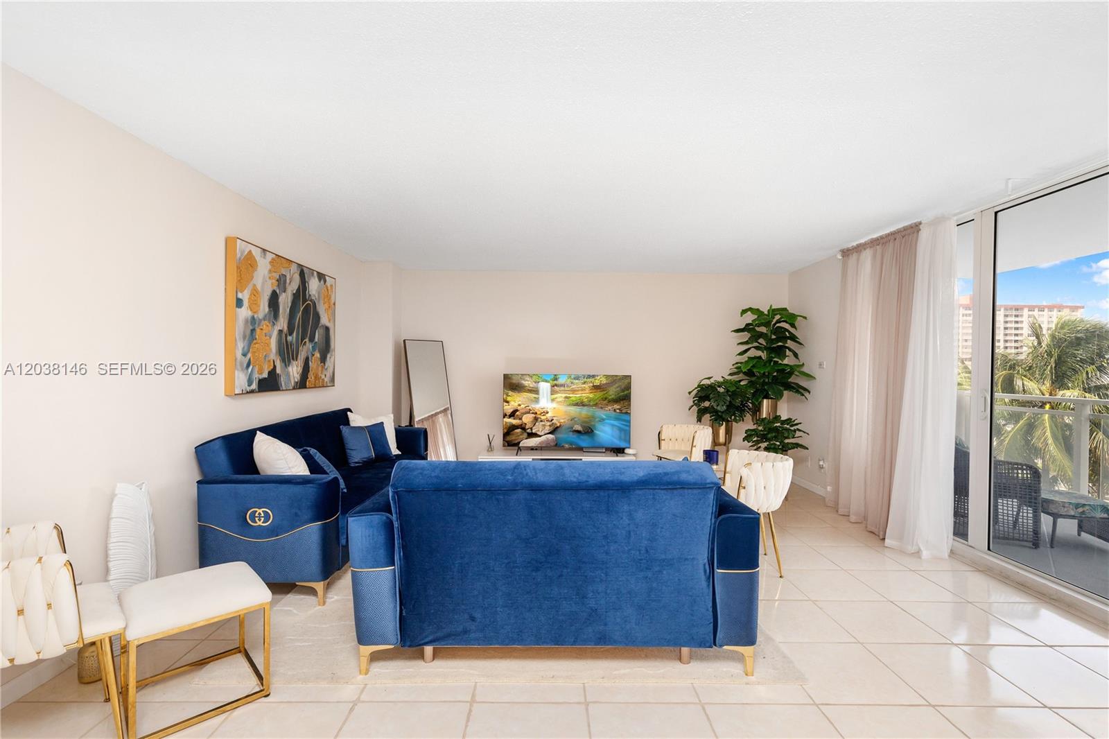 A living room features two blue velvet sofas, a television, and a balcony view — 2030 S Ocean Dr # 307, Hallandale Beach FL 33009, HALLANDALE BEACH, FL