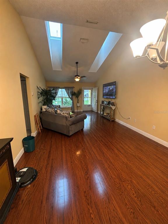 A living room with vaulted ceilings, skylights, hardwood floors, and a gray sofa — 41 WATER TRACK DRIVE, OCALA, FL