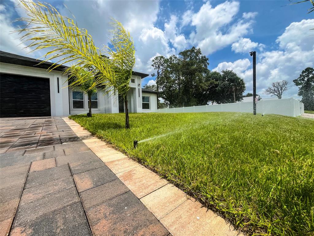 A sprinkler waters the front lawn of a modern house with a paved driveway — 2366 RIBBLE STREET, NORTH PORT, FL
