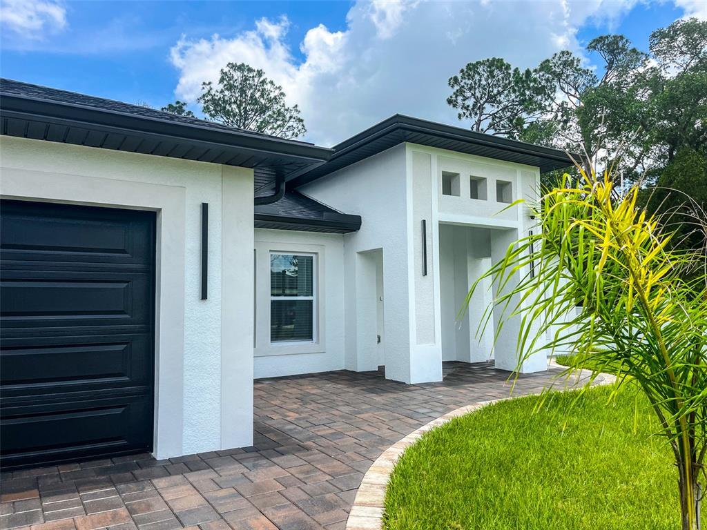 A modern white house exterior features a black garage door, paved driveway, and covered entryway — 2366 RIBBLE STREET, NORTH PORT, FL