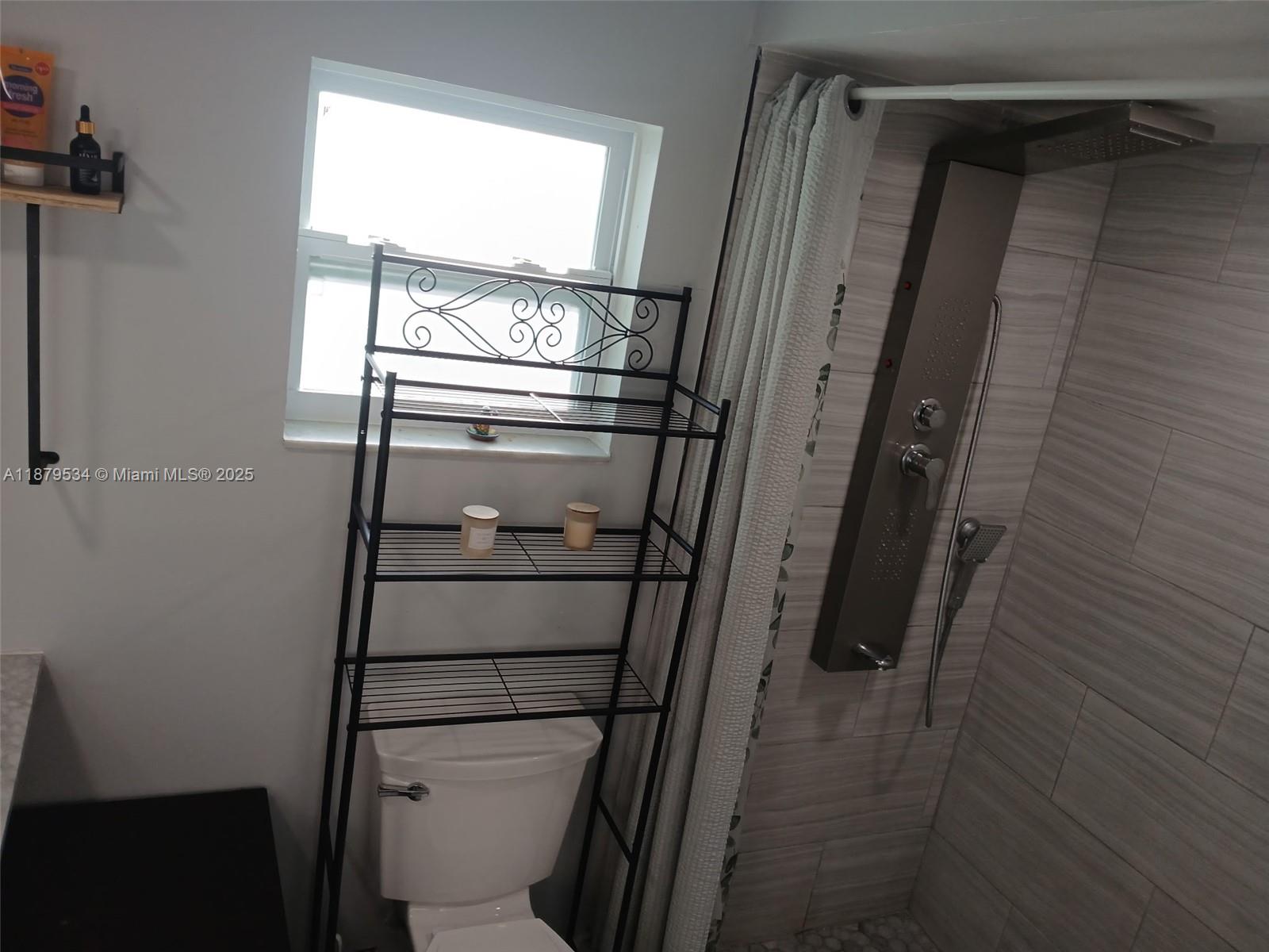 A bathroom features a toilet with a metal storage rack, a window, and a tiled shower — 11510 SW 182nd Ter # 2, Miami FL 33157, MIAMI, FL