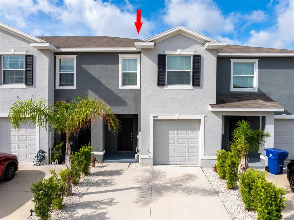The exterior of a two-story townhouse features a gray stucco facade and a garage — 34310 REDWOOD DAWN LANE, WESLEY CHAPEL, FL