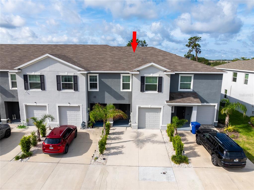An aerial view shows the exterior of a multi-unit townhouse complex with a red arrow — 34310 REDWOOD DAWN LANE, WESLEY CHAPEL, FL