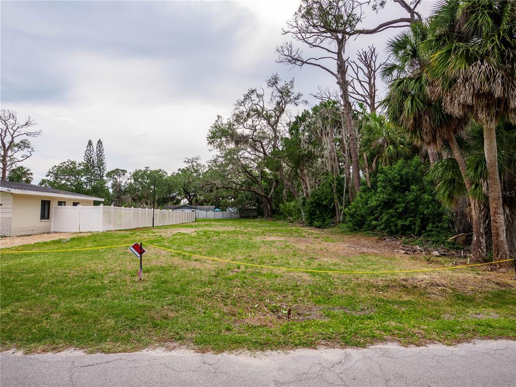A vacant, grassy residential lot is bordered by a white fence and mature trees — 7751 PIER ROAD, PORT RICHEY, FL