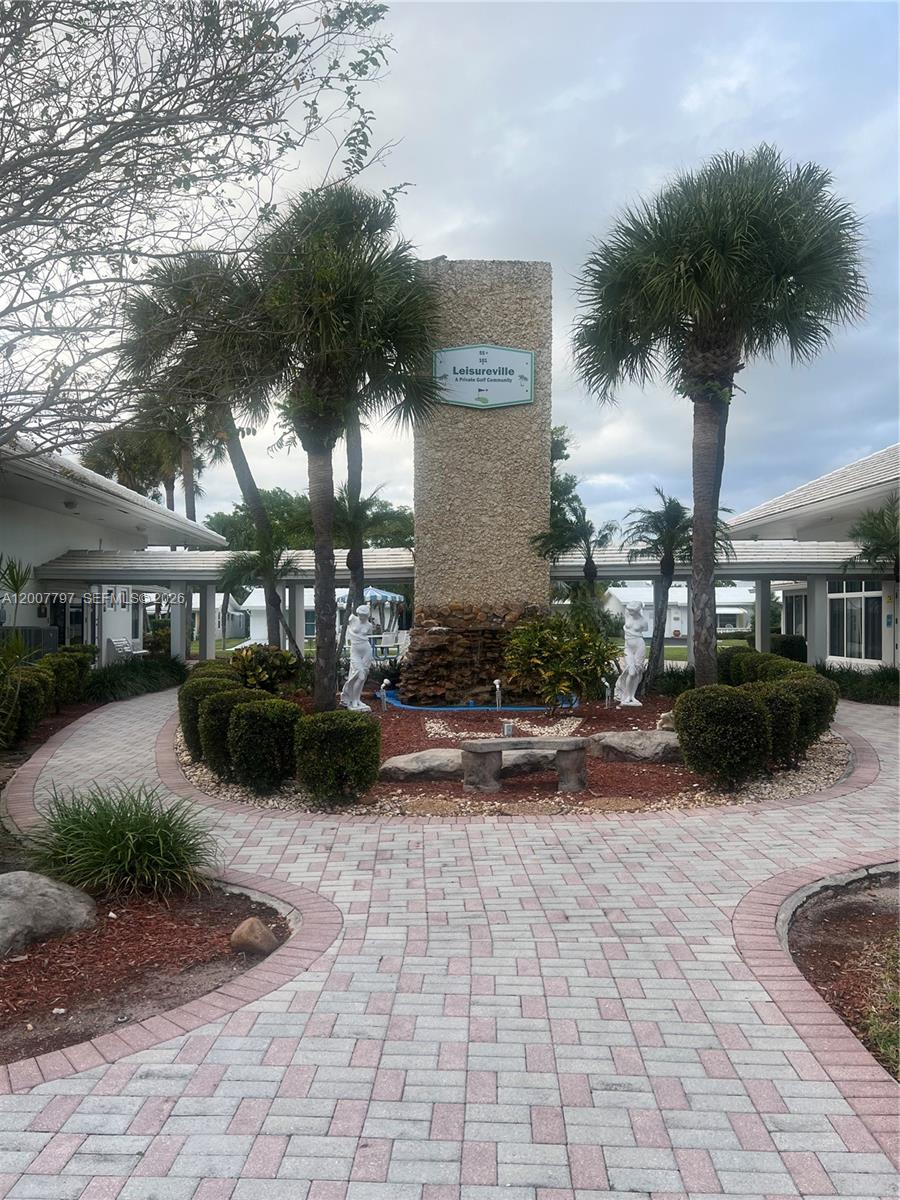 A paved walkway leads to a stone monument with a fountain and two palm trees — 2501 W Golf Blvd # 128, Pompano Beach FL 33064, POMPANO BEACH, FL