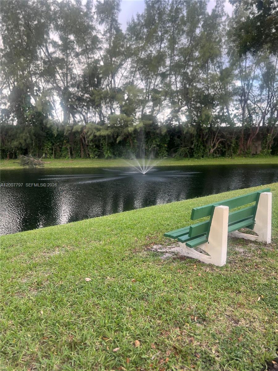 A green bench sits on a grassy lawn overlooking a pond with a water fountain — 2501 W Golf Blvd # 128, Pompano Beach FL 33064, POMPANO BEACH, FL
