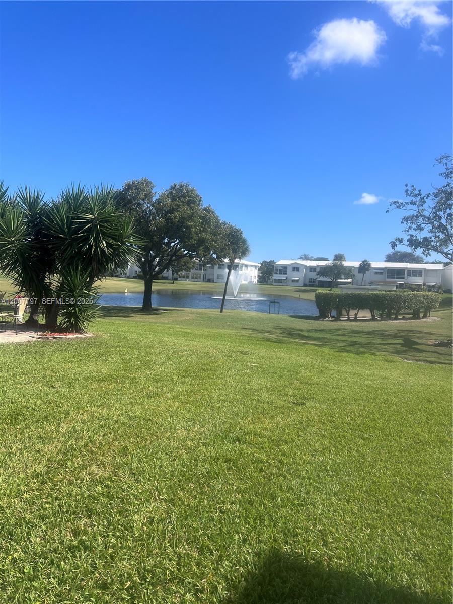 A grassy lawn leads to a pond with a fountain and residential buildings in the background — 2501 W Golf Blvd # 128, Pompano Beach FL 33064, POMPANO BEACH, FL